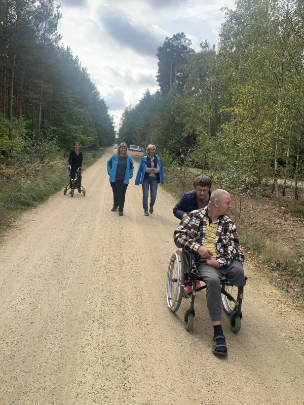 Mieszkańcy spacerują drogą - po bokach las
