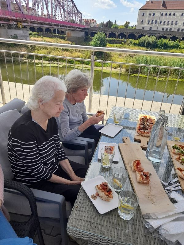 Mieszkanki przy stole jedzą pizzę w tle rzeka Odra