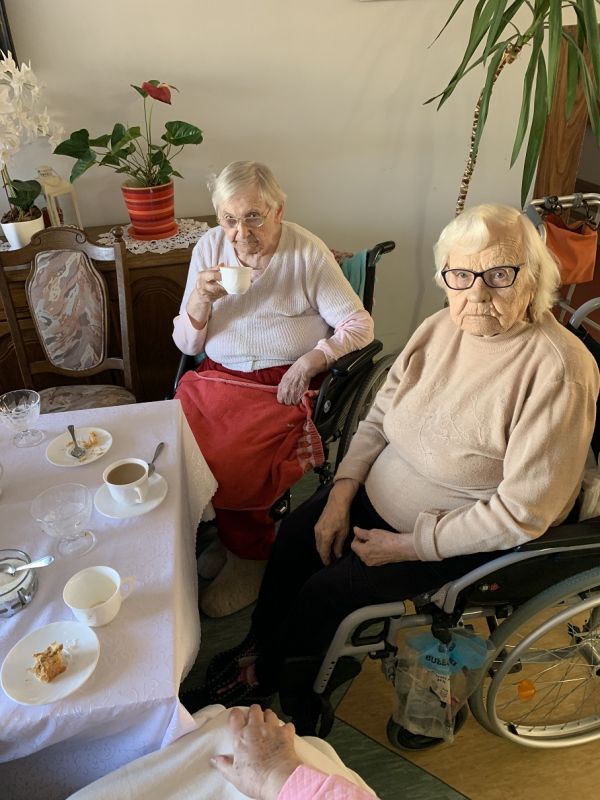 Dwie mieszkanki na wózkach inwalidzkich przy stole piją kawę