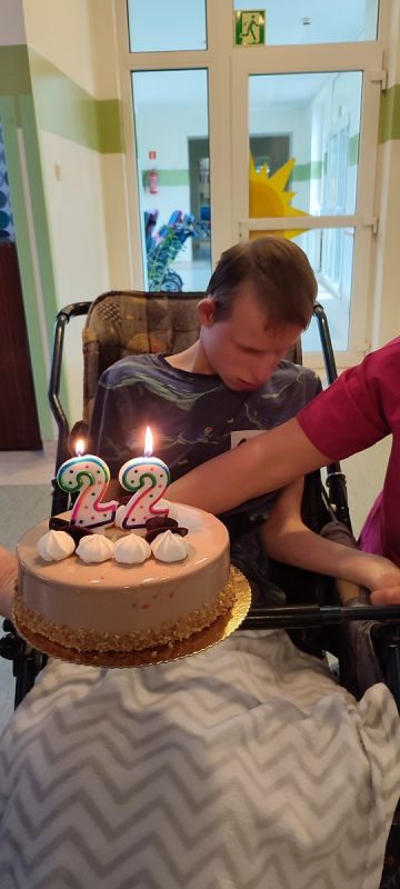 Podopieczny siedzi w wózku,  przed nim tort urodzinowy z cyfrą 22 