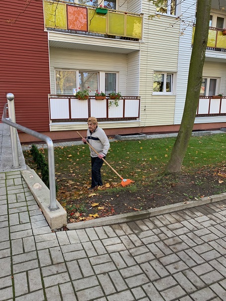 Mieszkaniec DPS podczas grabienia liści przed budynkiem