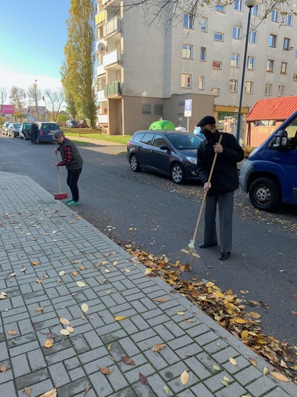 Dwoje mieszkańców zmiata liście z ulicy przed DPS