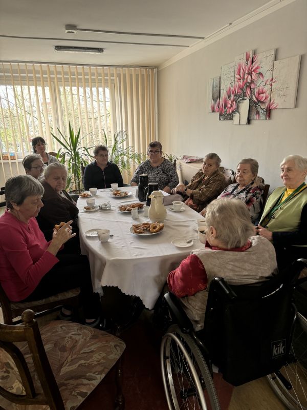 Grupowe zdjęcie mieszkańców przy stole. Na stole słodkie wypieki i kawa