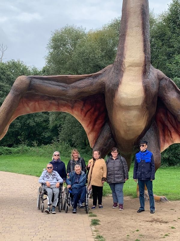 Grupa mieszkańców stoi pod figurą dinozaura